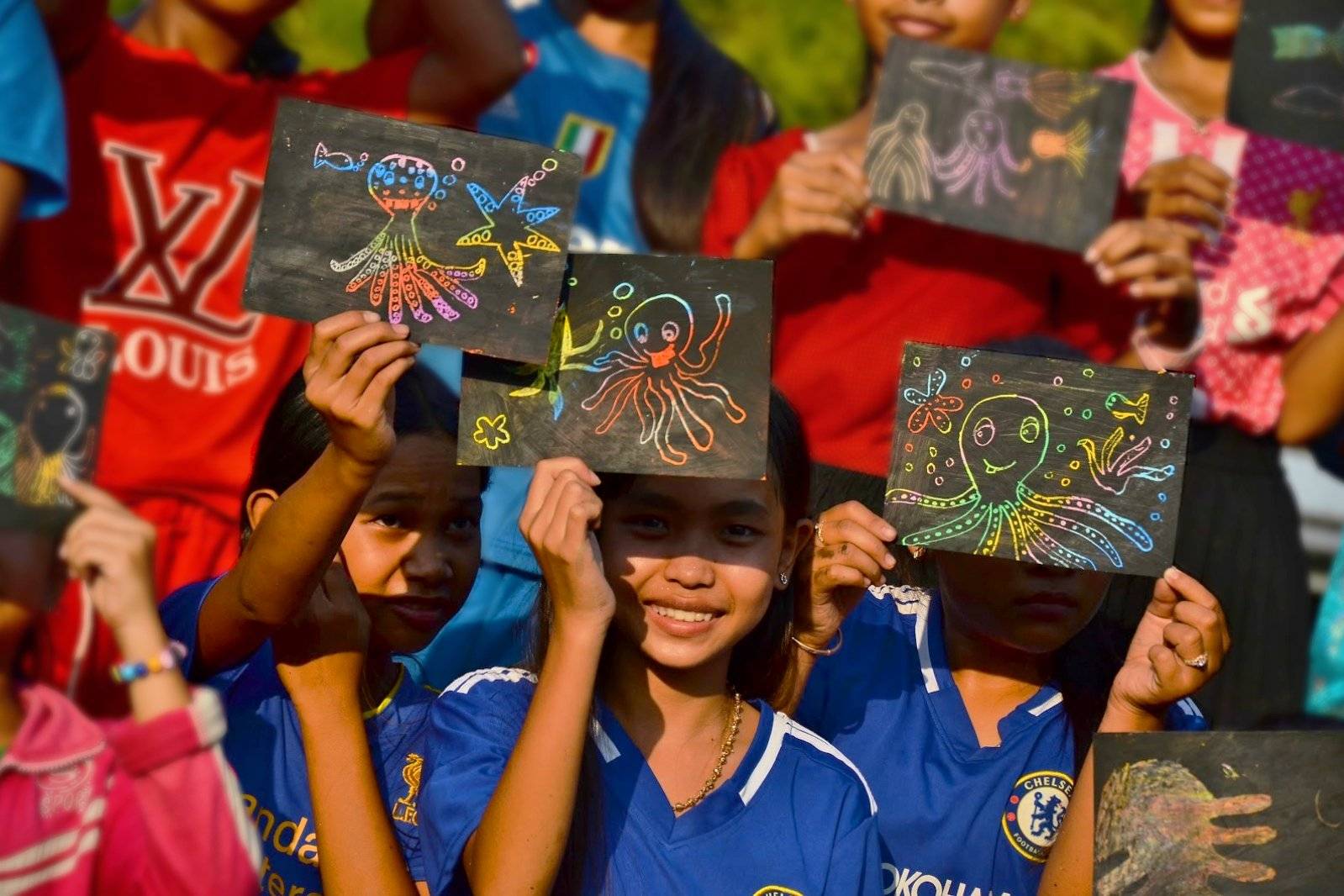 Cambodian young girls showing their octopus drawings at the end of our outreach session